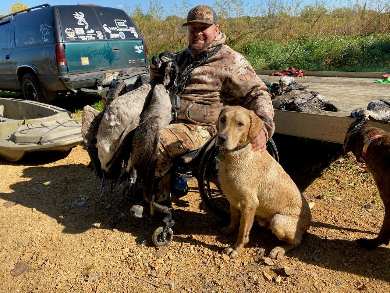 A seated hunter with a yellow Labrador and a pile of geese at the end of a hunt.