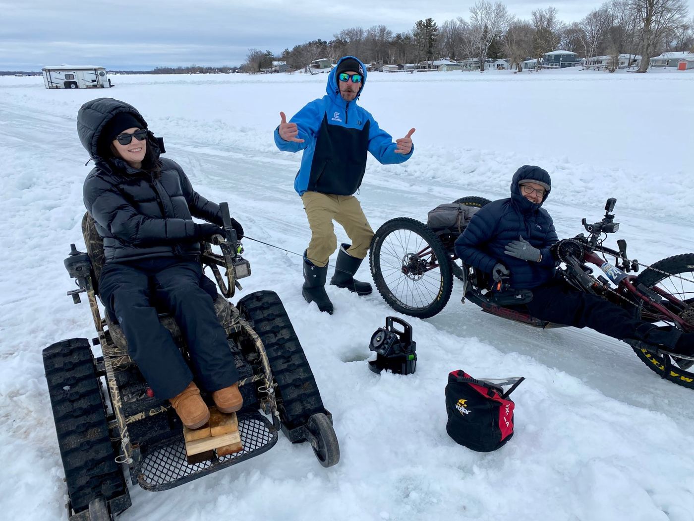 Participants in tracked wheelchairs and volunteers gather on a frozen Minnesota lake.